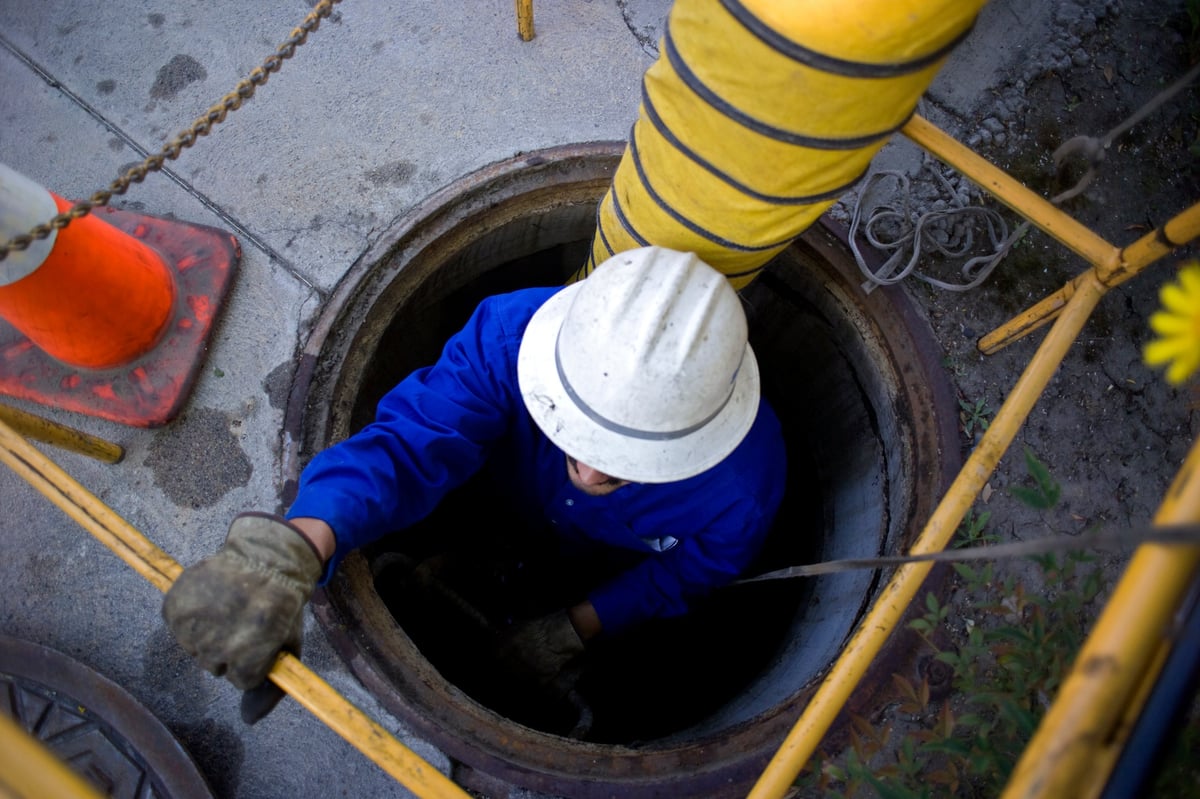 Worker in safety harness descending into underground lift station vault