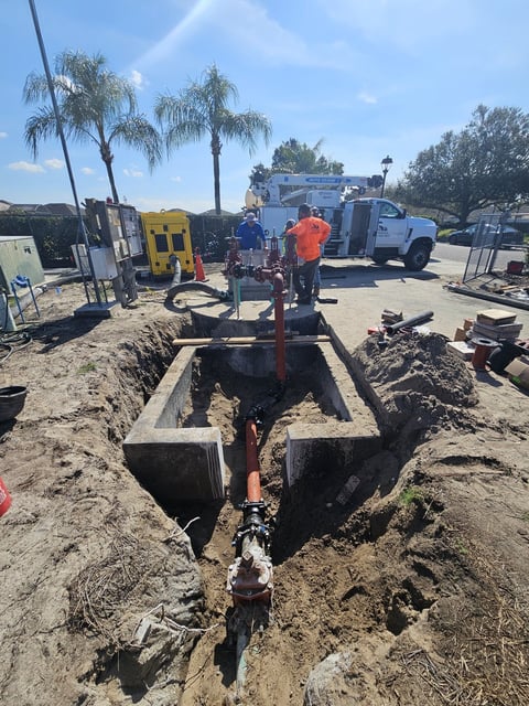 Construction worker in orange vest operating underground utility equipment in excavated trench