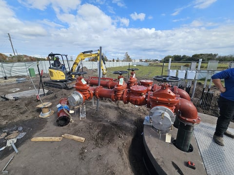Construction site with red industrial pipes, yellow excavator, and workers