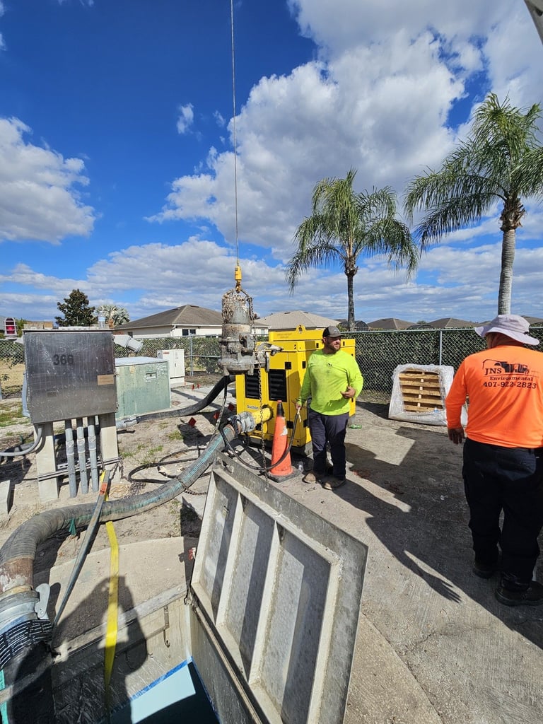 Construction workers in safety vests operating yellow machinery on a concrete pad at a job site with palm trees