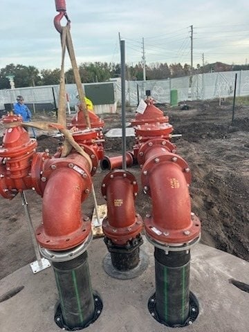 Red fire hydrants on concrete foundation at industrial site with rigging equipment and metal fencing in background