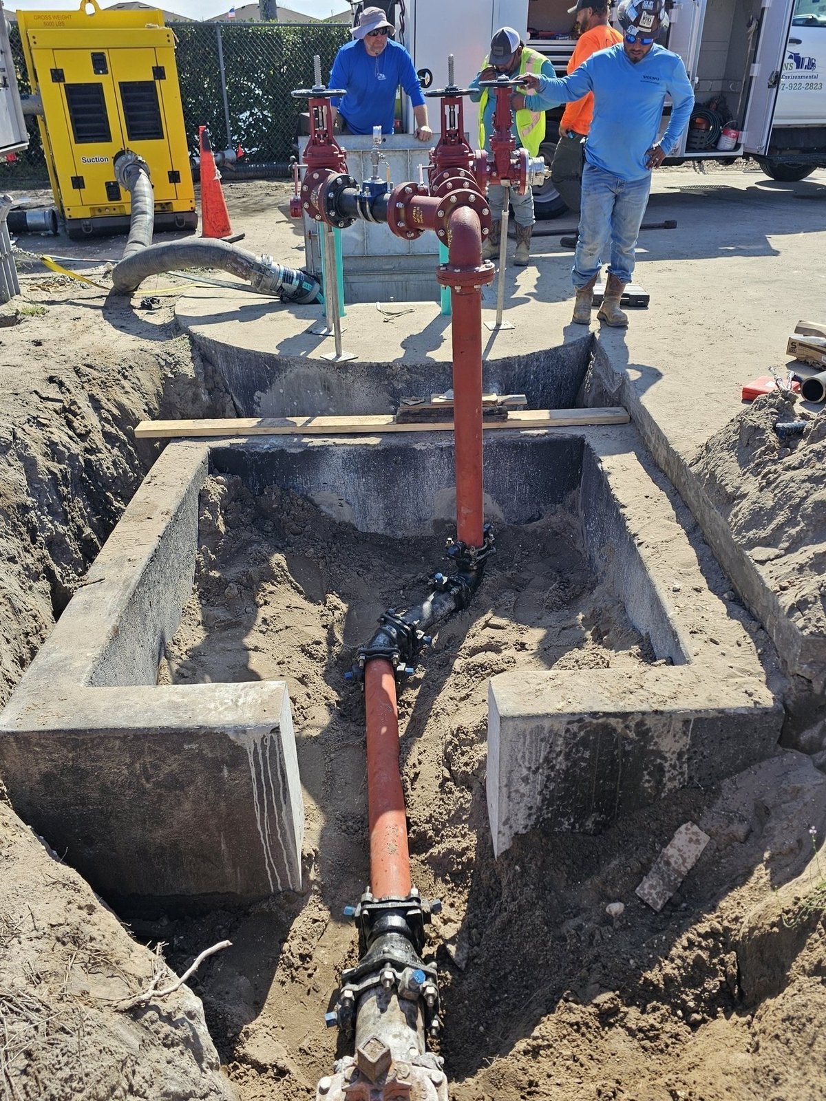 Construction workers installing underground utility pipes and valve system in concrete trenches at a job site
