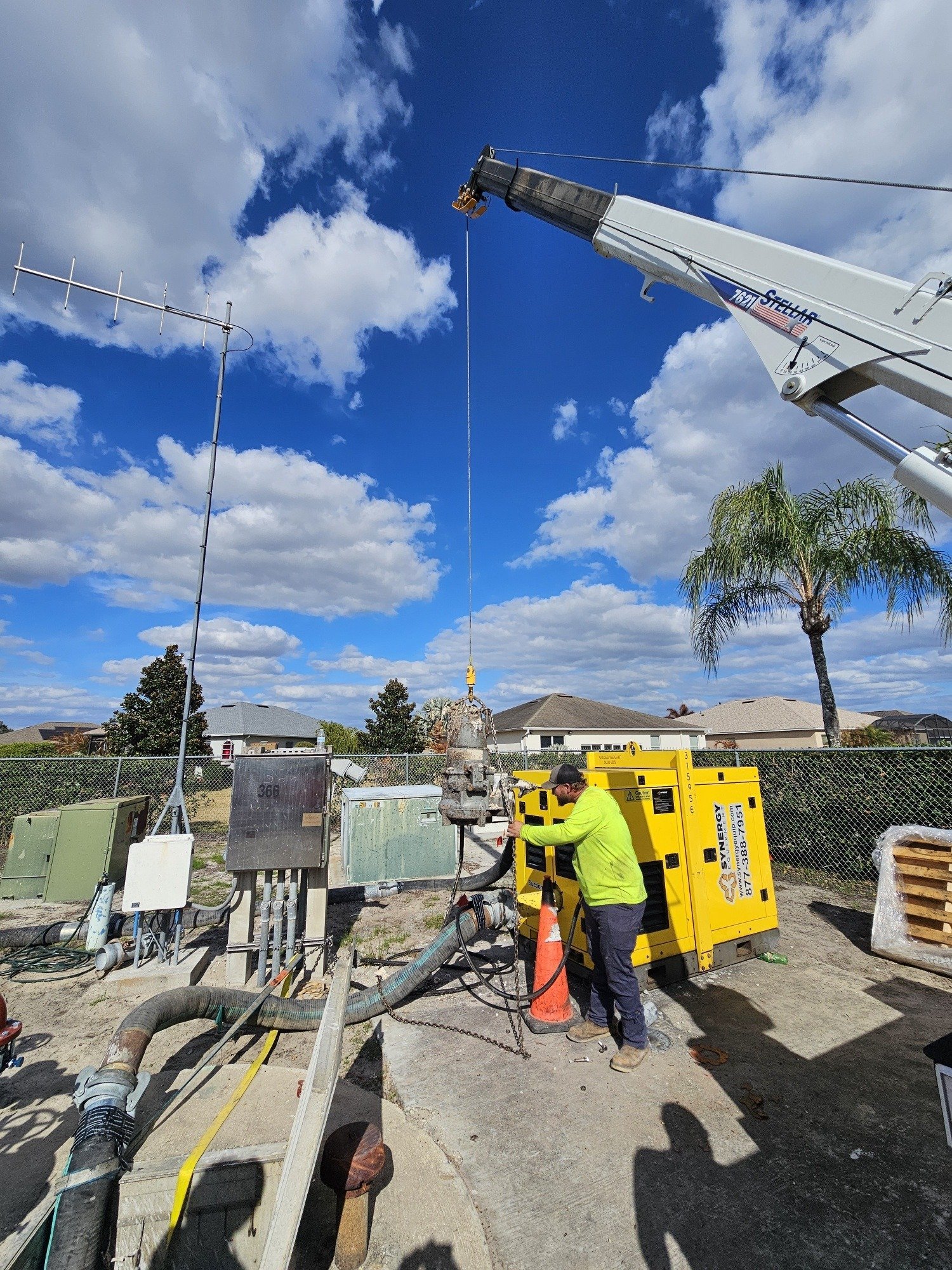 Worker in high-visibility gear operating a boom lift at a construction site under clear blue sky