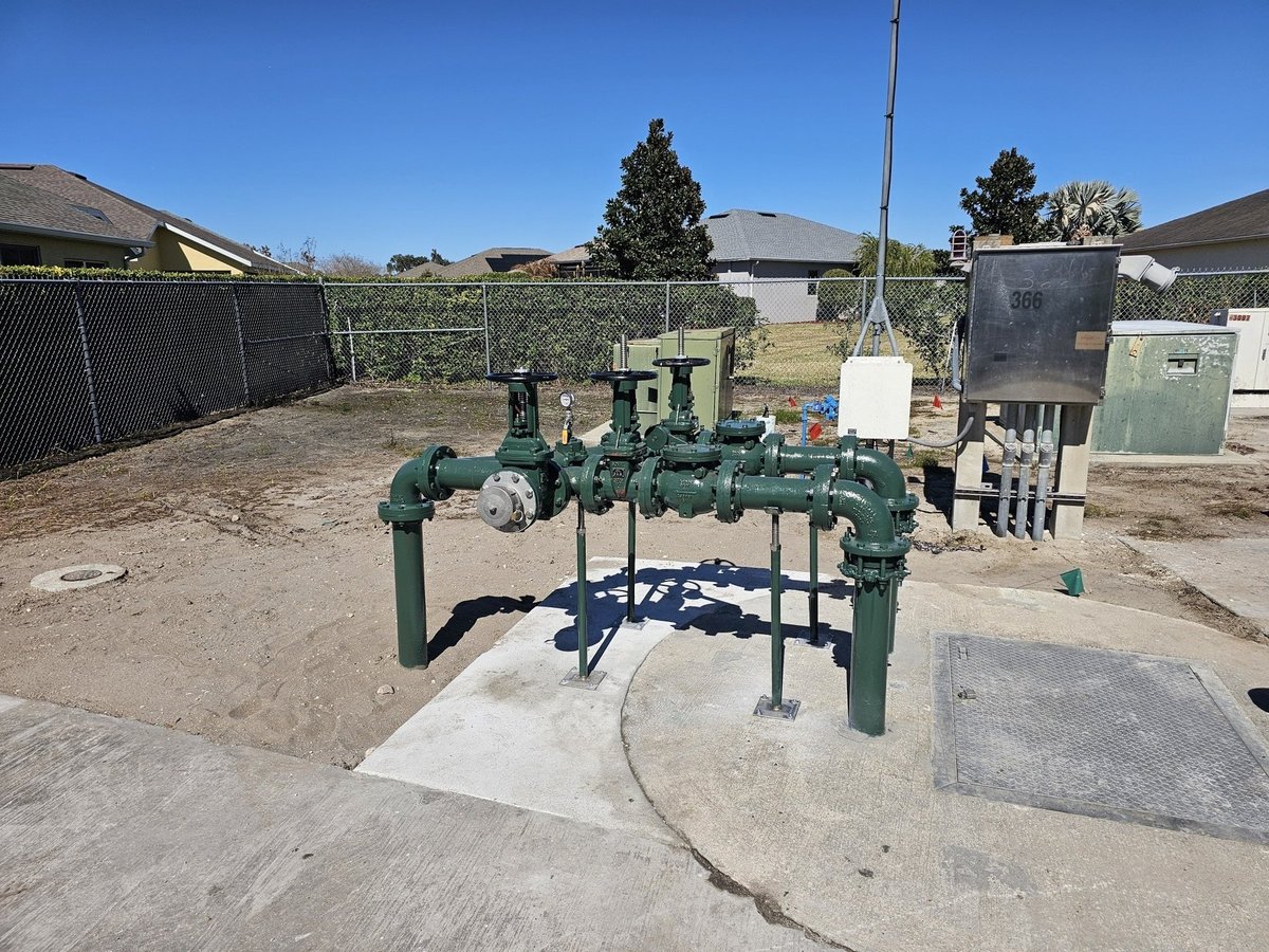 Green industrial water pump and piping system installed on concrete pad in outdoor facility with residential houses in background