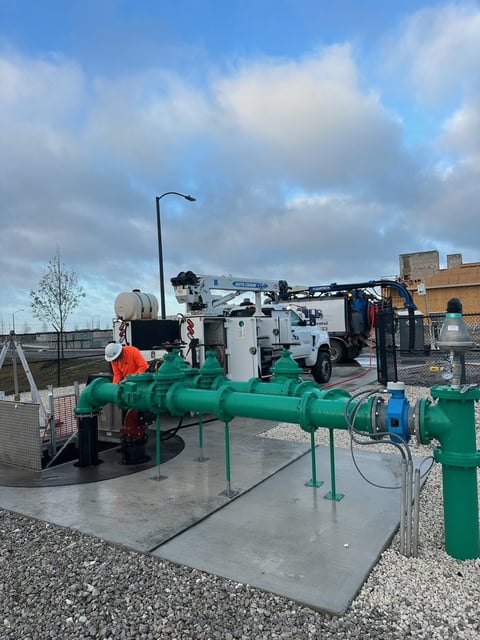 Utility truck with green pipes and equipment on concrete pad at industrial facility